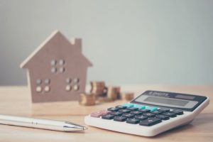 Calculator with wooden house and coins stack and pen on wood table. Property investment and house mortgage financial concept